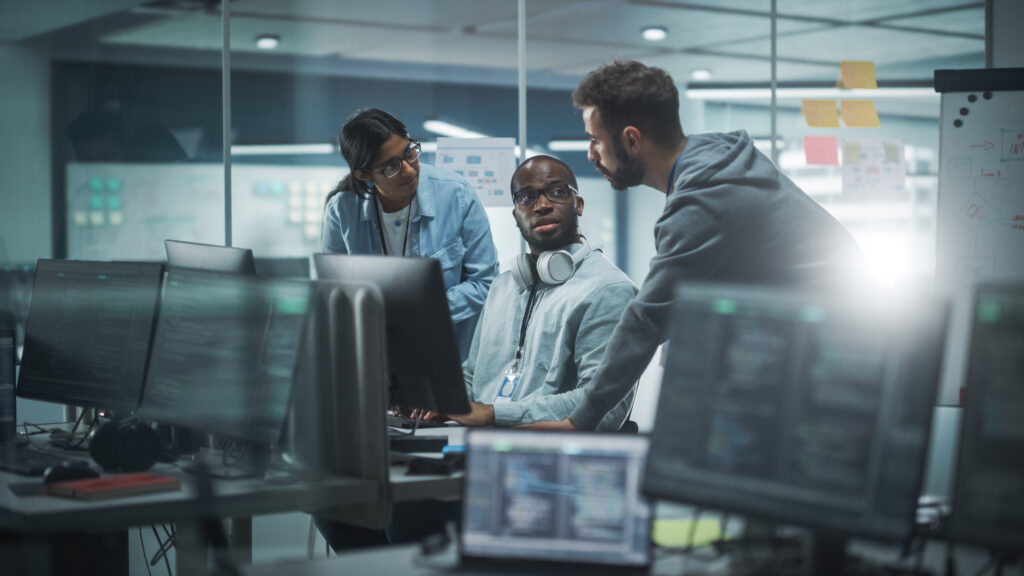 Três profissionais se reúnem em volta de um computador enquanto discutem estratégias.