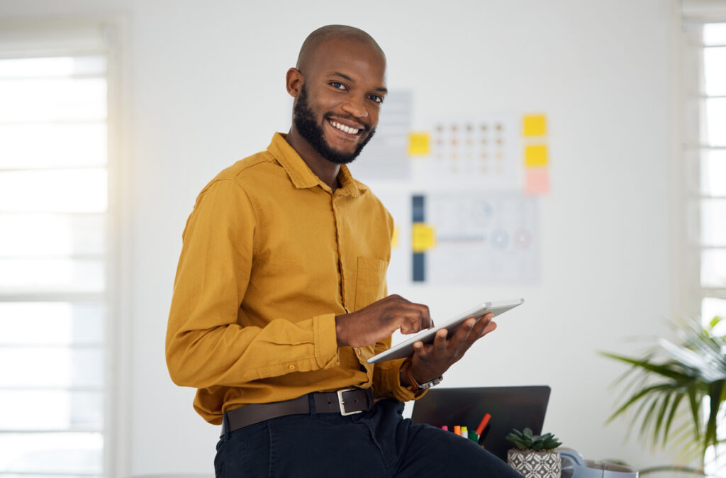 homem de camisa social ocre sorrindo e mexendo em um tablet